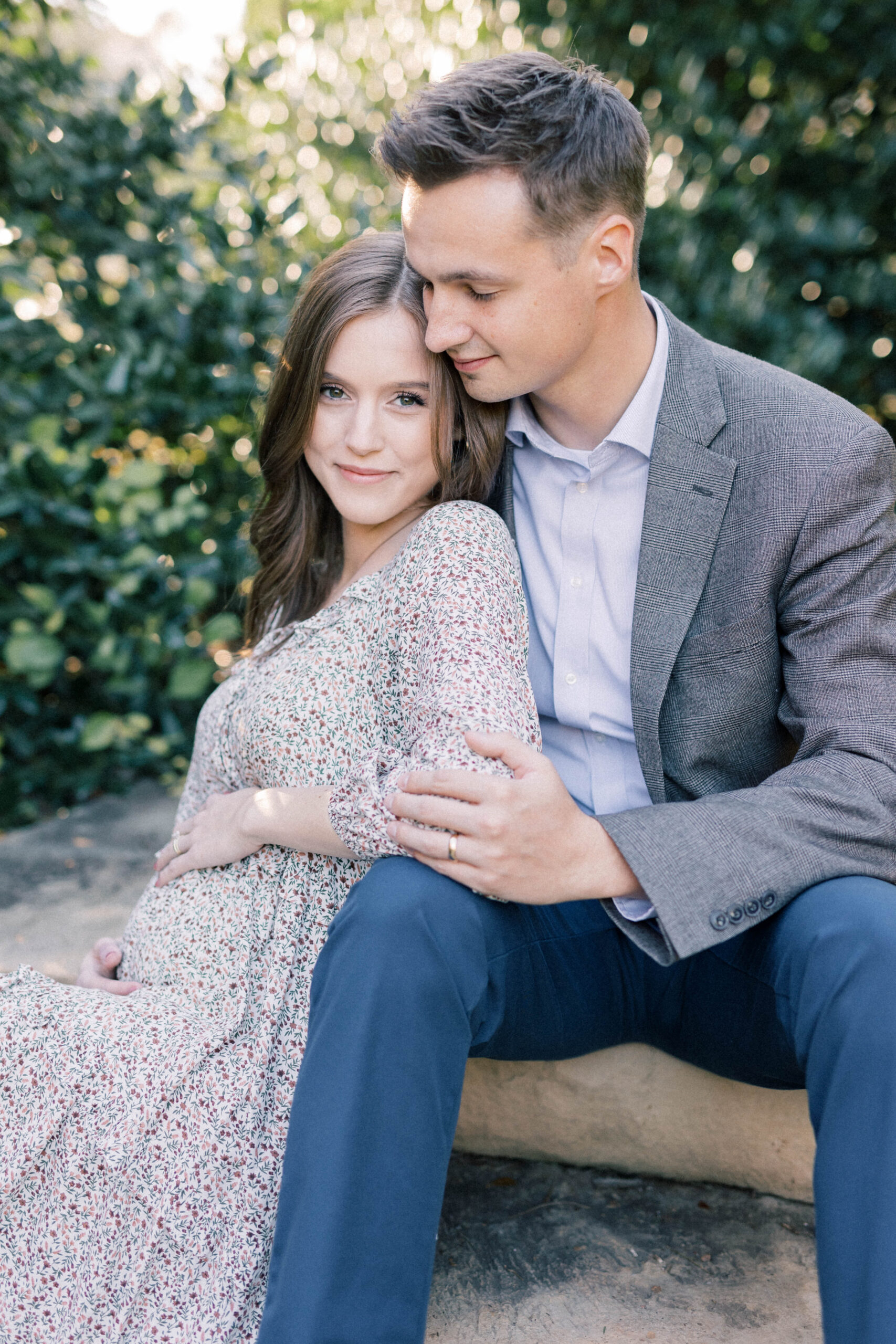 husband and wife sitting on stairs in knoxville botanical garden. women holding baby belly and husband holding her arm.