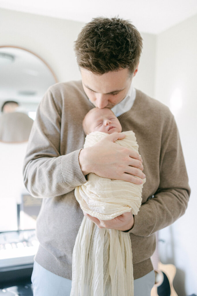 knoxville newborn photographer. dad holding swaddled newborn baby in front of him kissing babys head