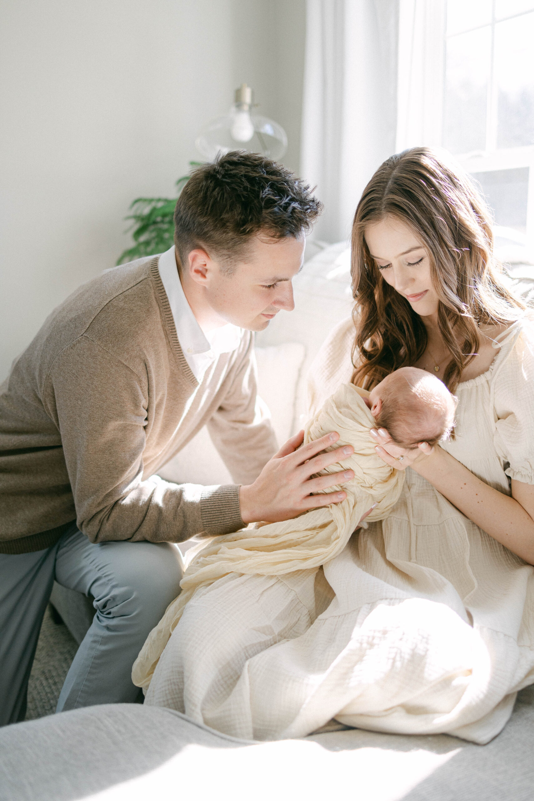 man and women admiring new baby. lots of sunlight and cream tones. knoxville newborn photographer