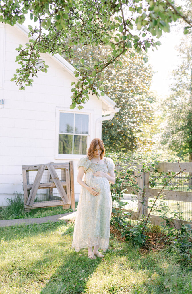 pregnant women standing under lush green tress in a beautiful green dress holding her belly and smiling down at her baby bump. lots of backlight Knoxville TN lifestyle fertility photographer