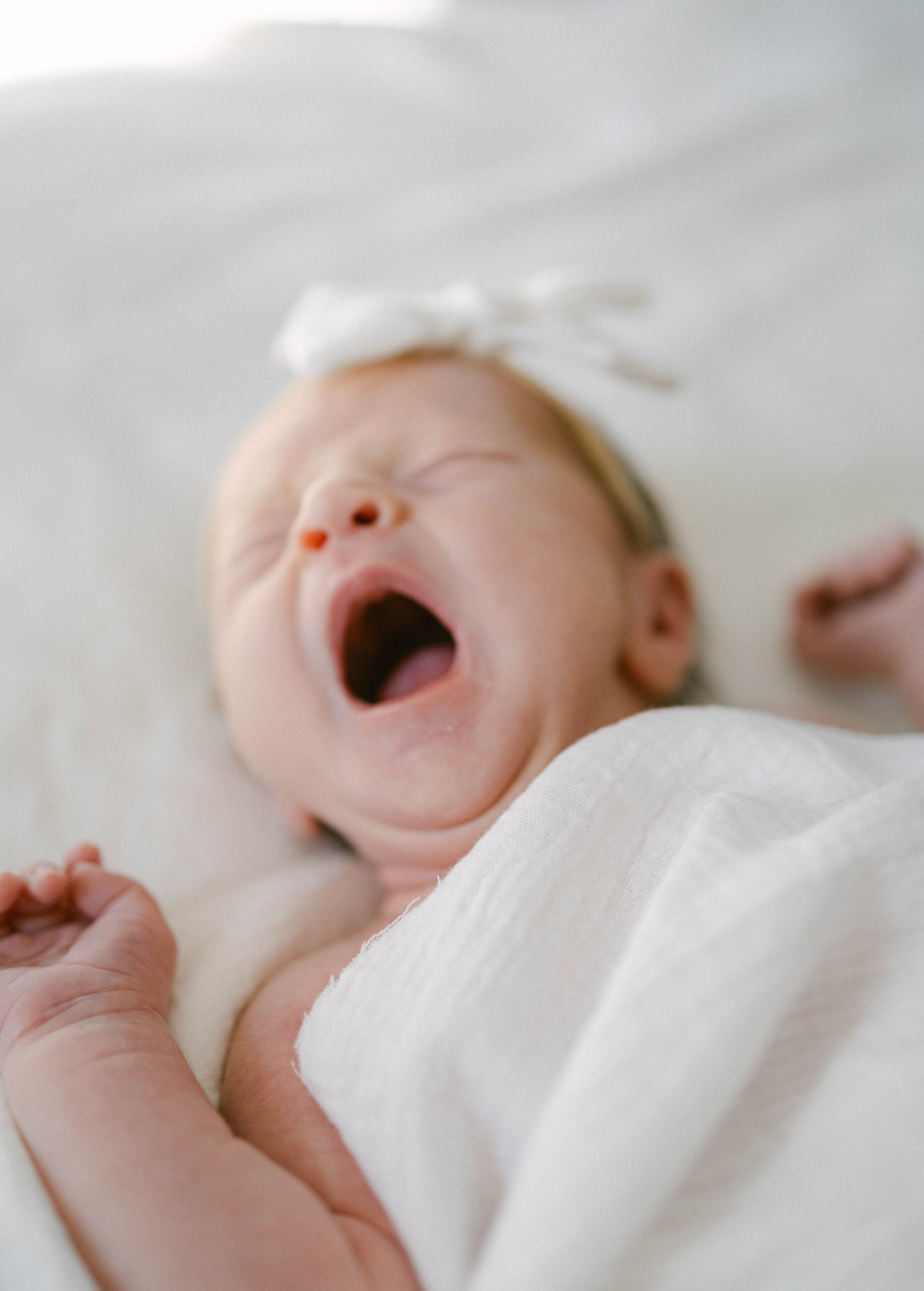sleepy baby yawning wrapped in white cloth. knoxville newborn photographer. when to book newborn photographer knoxville