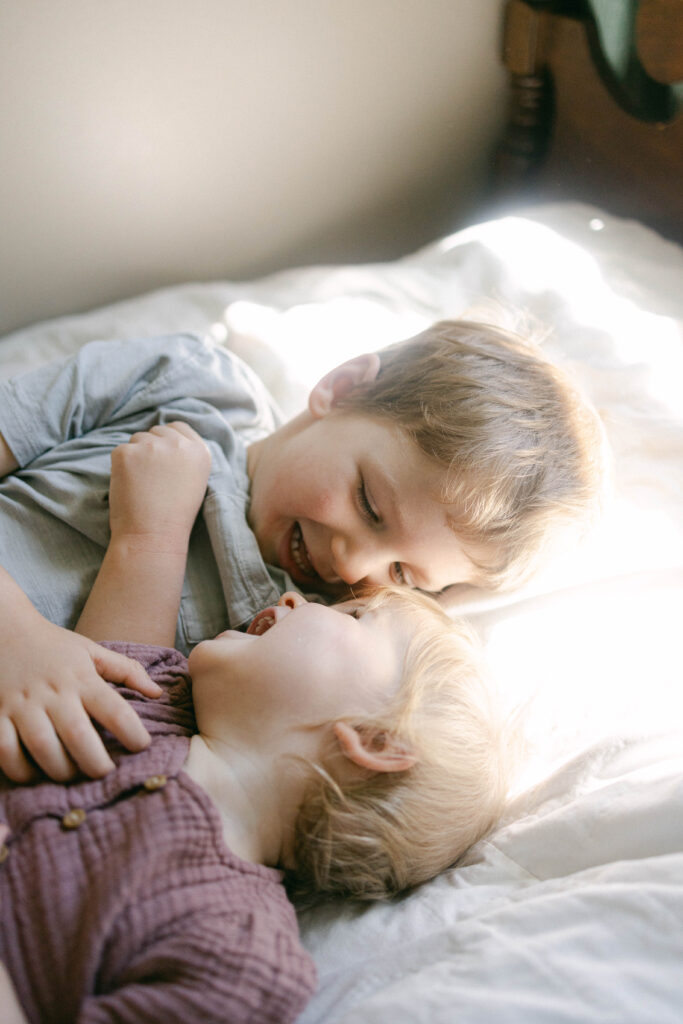 toddlers playing together and laughing on bed during an in home family session in knoxville tn