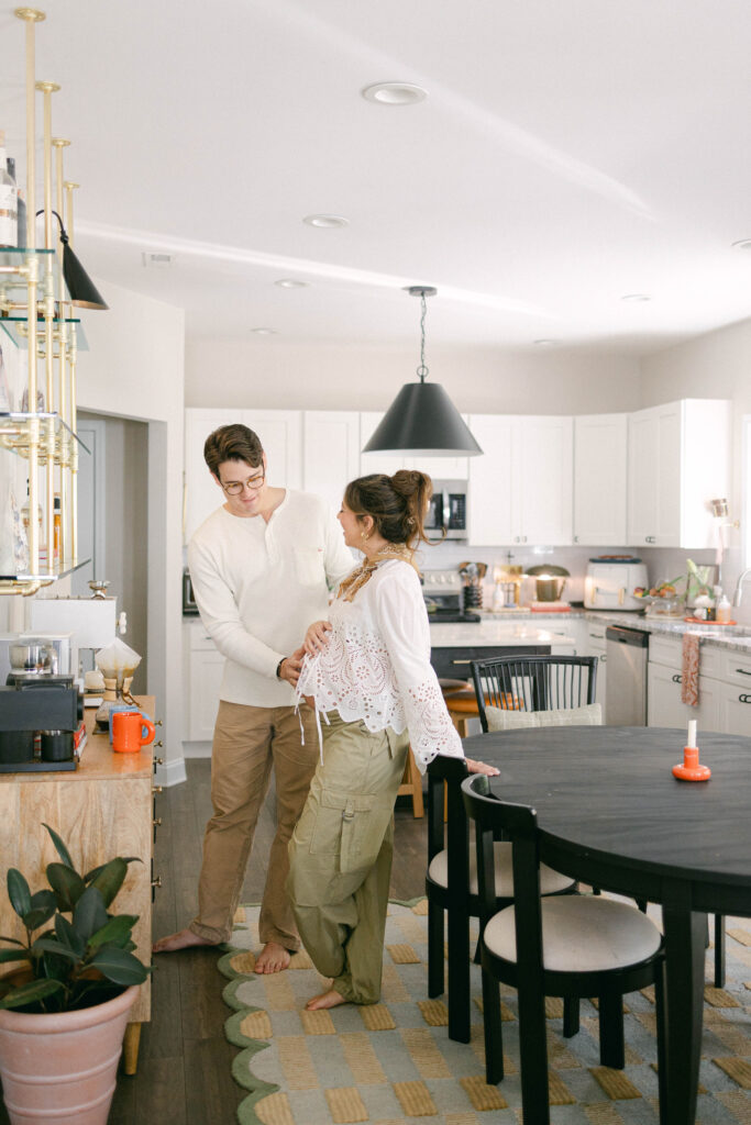 Expectant mother with husband standing by a window during an in-home maternity photography session in Knoxville.