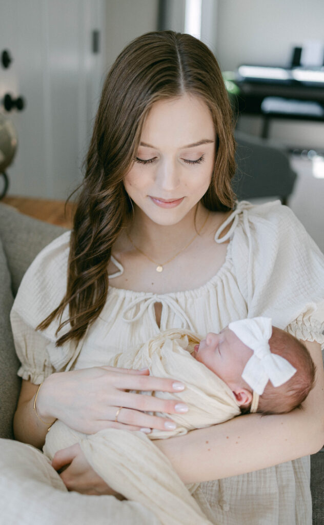 Mother holding her newborn baby near a window during a lifestyle newborn photography session.