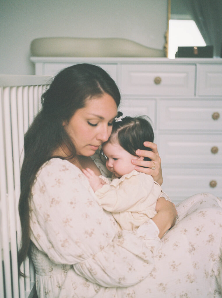 Mother cuddling her newborn in a softly lit nursery during an in-home newborn photography session in Knoxville, Tennessee. film photography