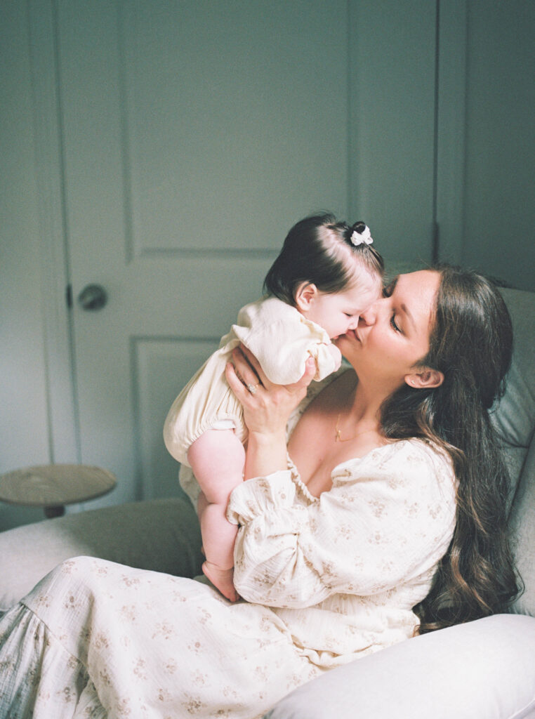mom wearing comfy cream postpartum dress while kissing baby's cheek by natural window light in home knoxville family photographer